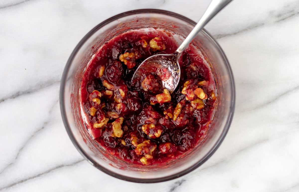 Cranberry sauce and walnuts mixed together in a glass bowl.