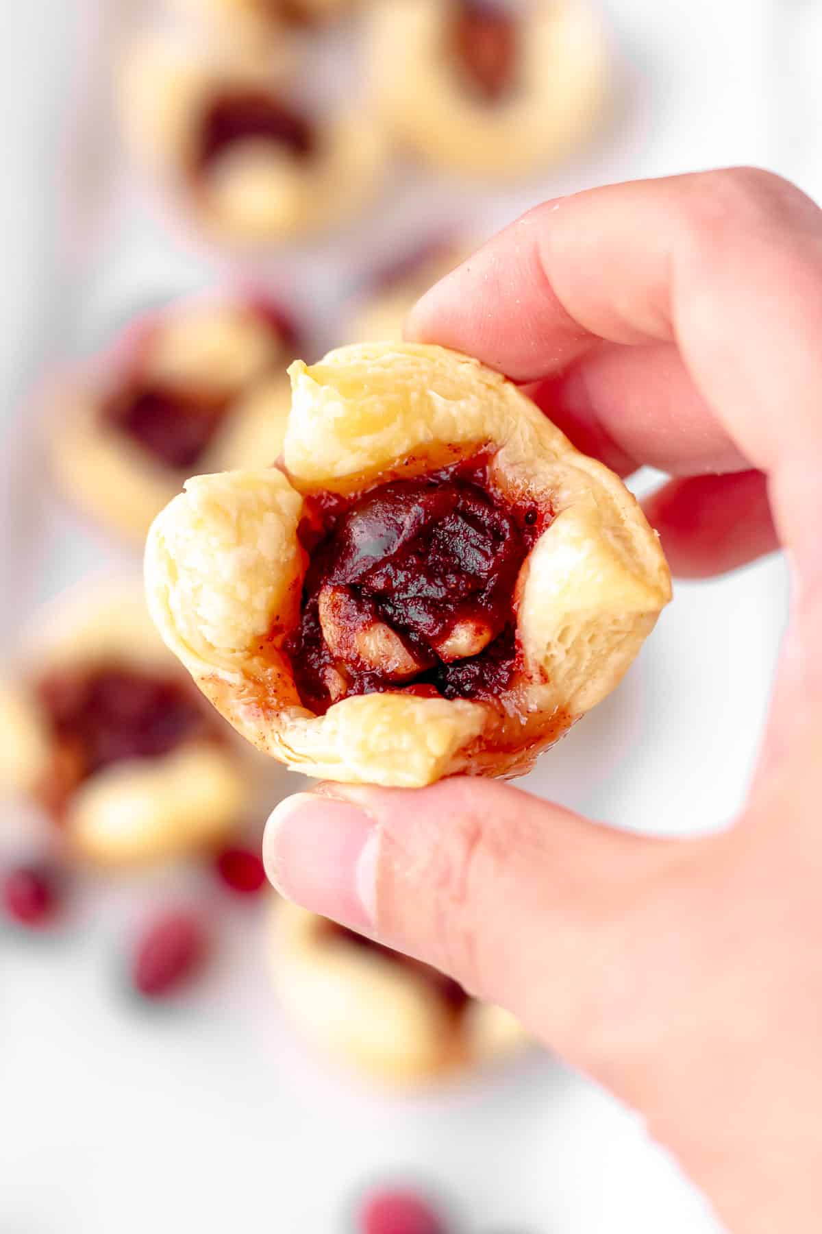 A hand holding up a cranberry walnut puff pastry cup.