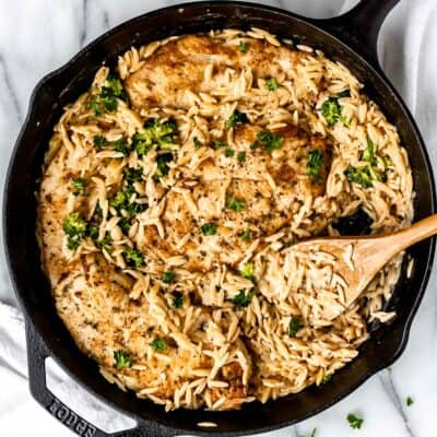Creamy parmesan orzo chicken and orzo pasta with broccoli and a wood spoon in it.