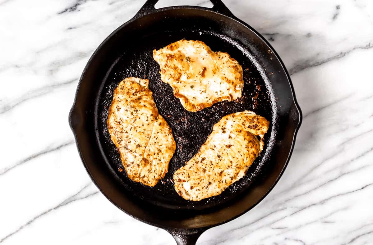Three chicken breasts cooking in a skillet.