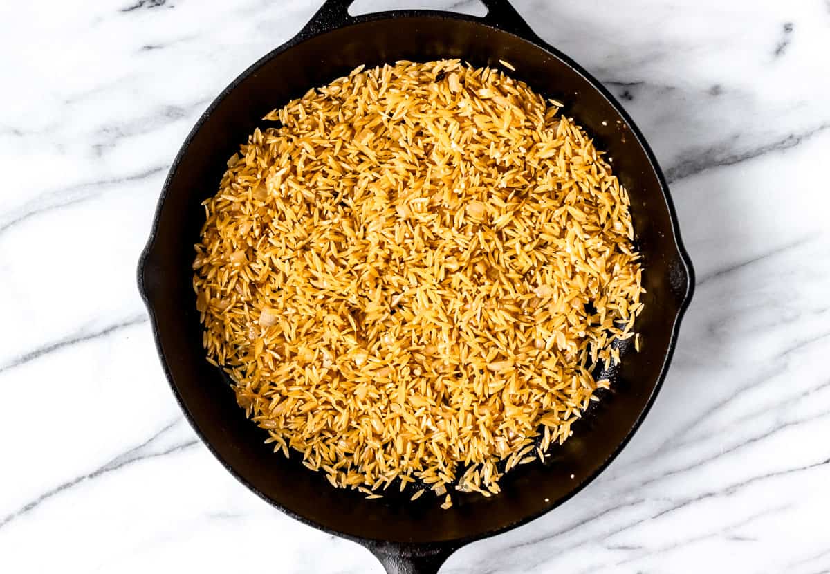 Toasted orzo in a cast iron skillet.