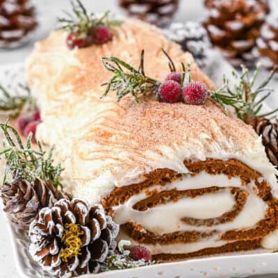 A gingerbread yule log cake decorated with pine cones, sugared cranberries and rosemary.
