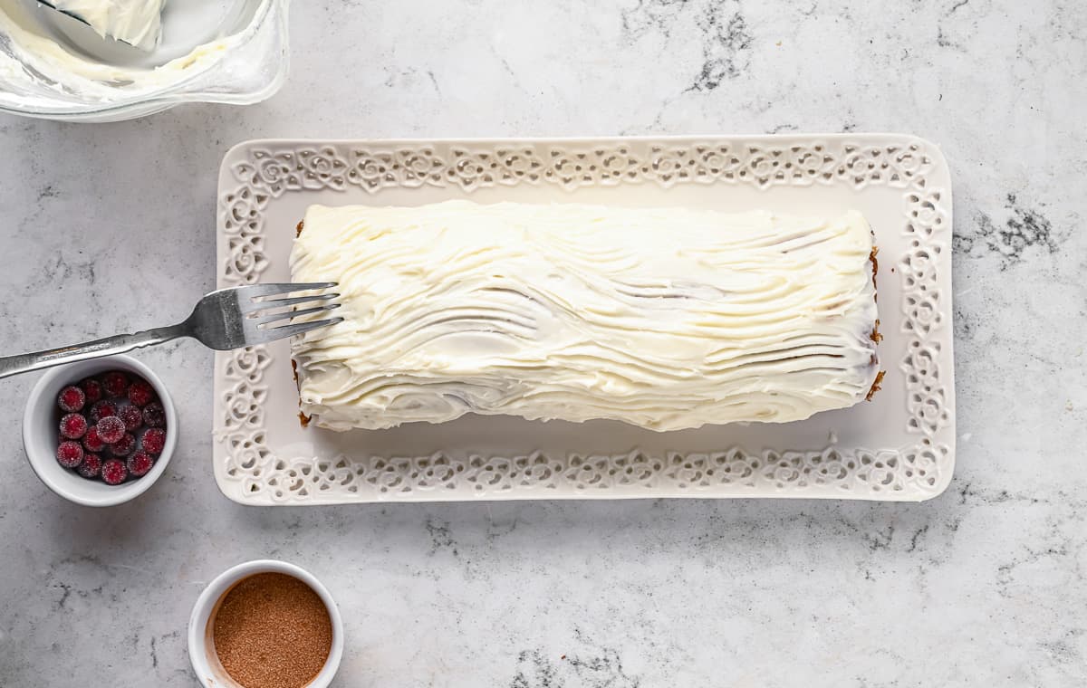 A frosted gingerbread yule log cake with a fork dragging lines into it to make it resemble a log.