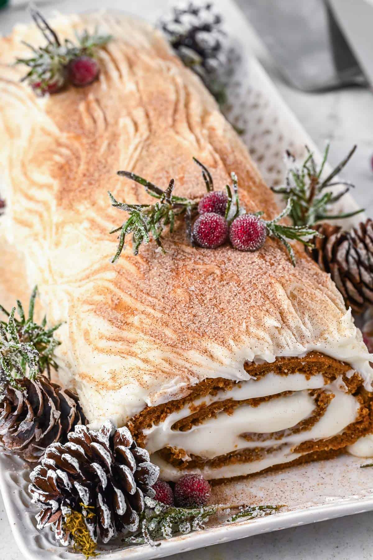 A gingerbread yule log cake decorated with pine cones, sugared cranberries and rosemary.