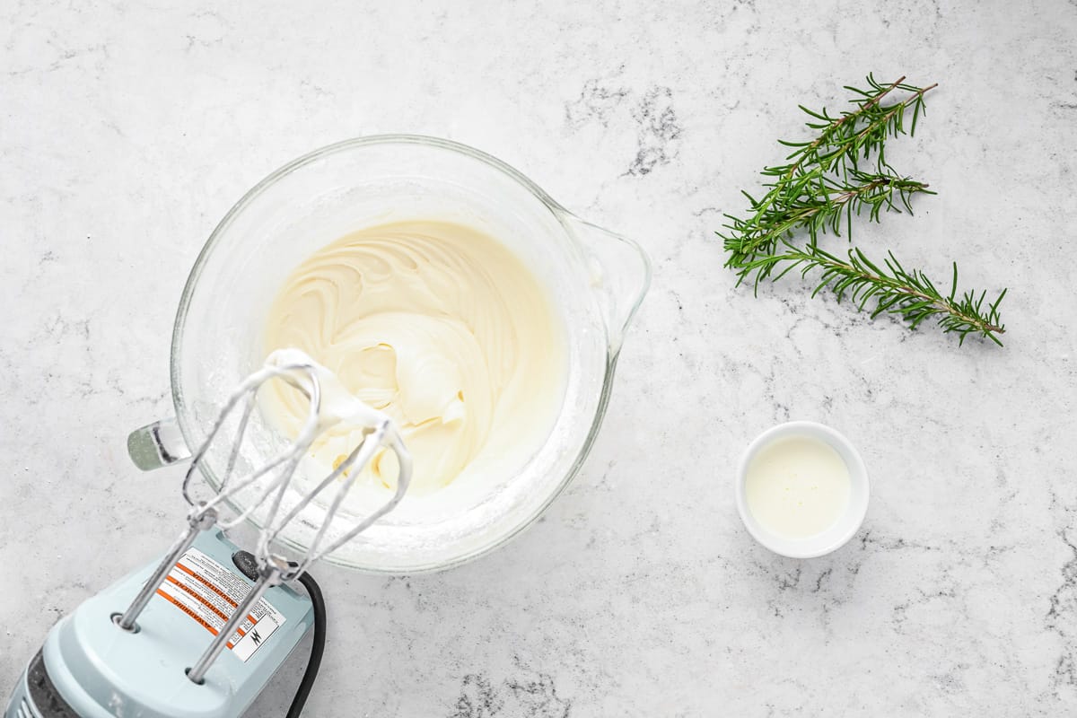 Rum cream cheese frosting in a mixing bowl with rosemary next to it.