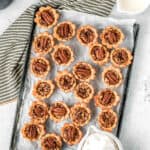 Overhead of a tray of mini pecan pies with whipped cream in a bowl and a towel around it with text overlay.