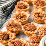 Mini Pecan Pies on a tray with a striped towel next to it.
