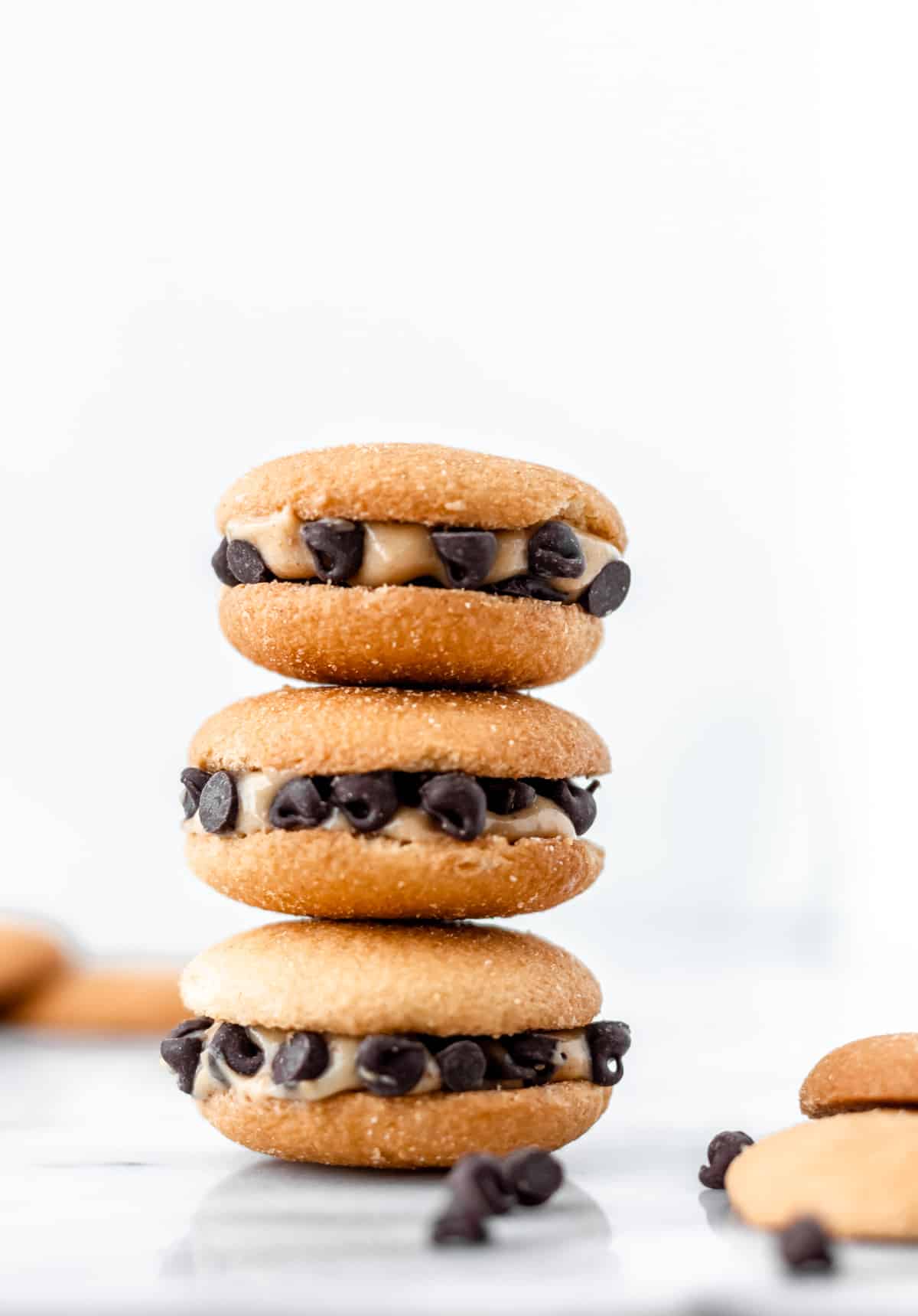 A stack of three peanut butter chocolate chip Nilla wafer sandwich cookies with extra cookies and mini chocolate chips around it.