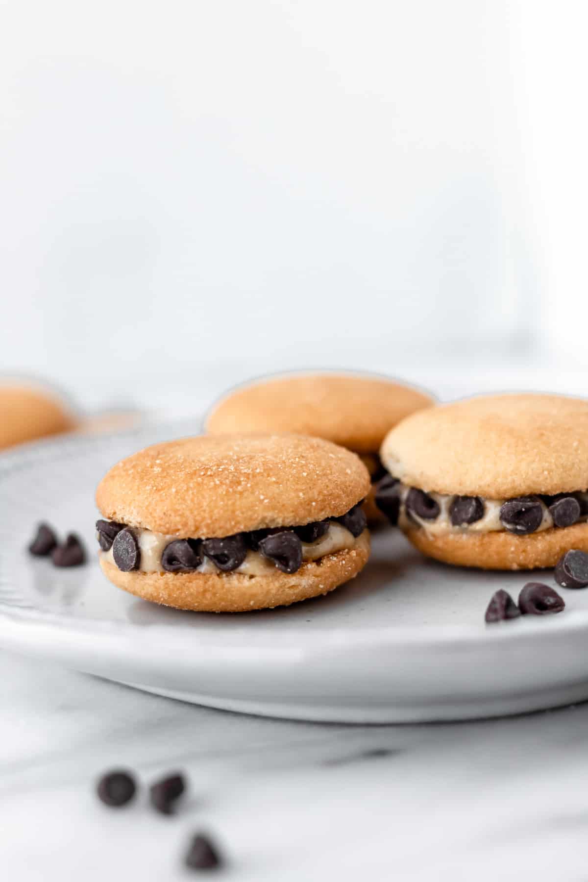 Three peanut butter chocolate chip Nilla wafer sandwiches on a plate with mini chocolate chips in the front.