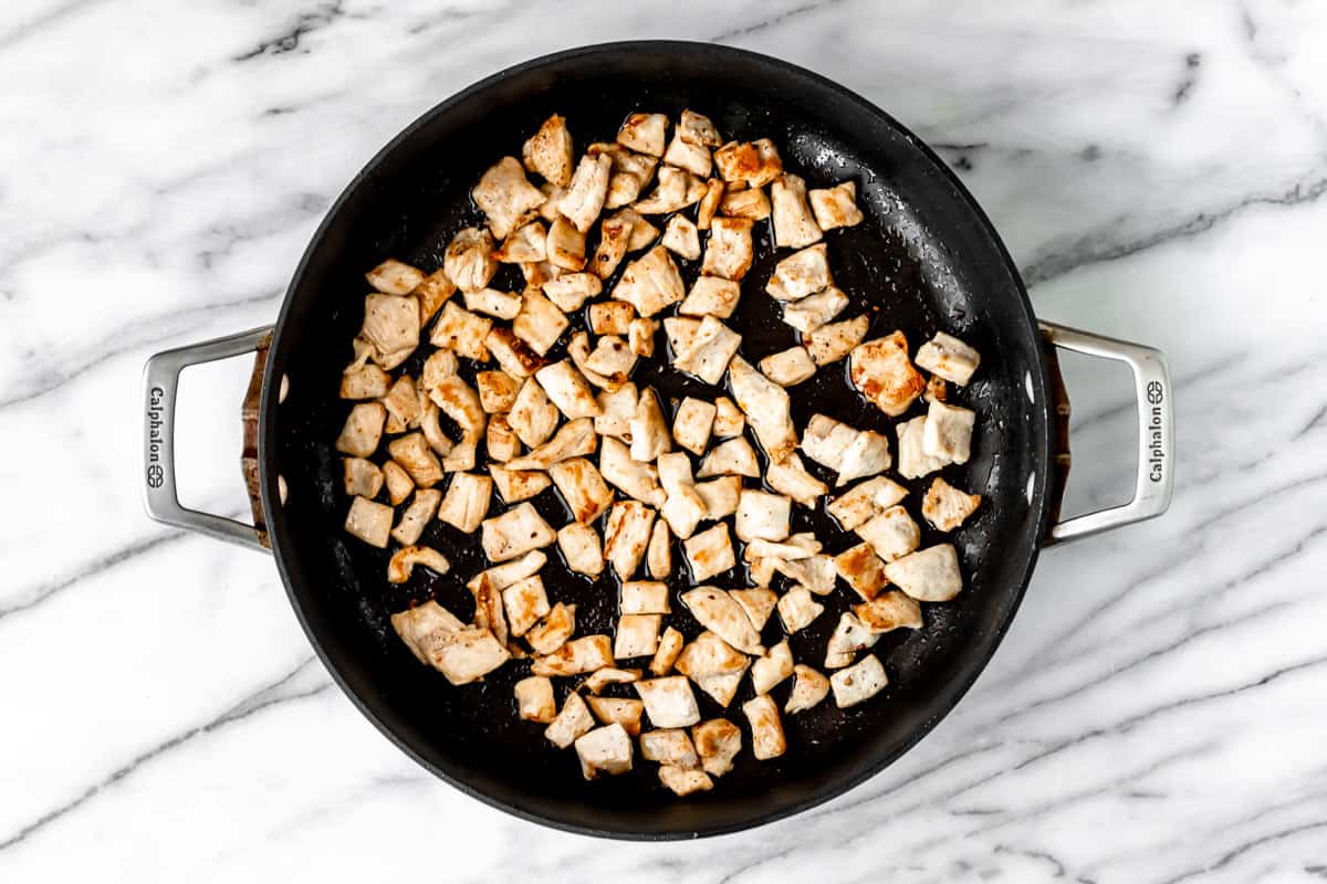 Cubes of cooked chicken in a black skillet.
