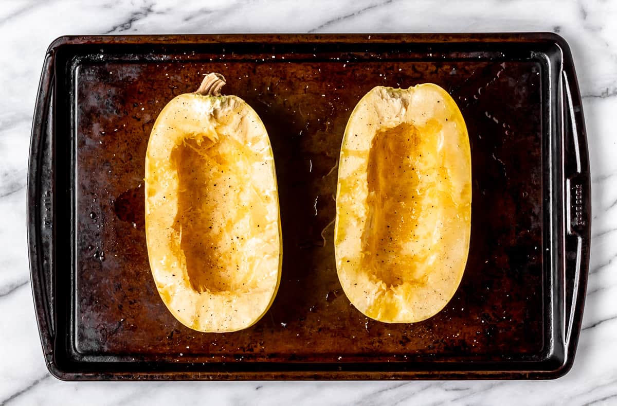 Raw spaghetti squash cut in half with seeds removed on a baking sheet.