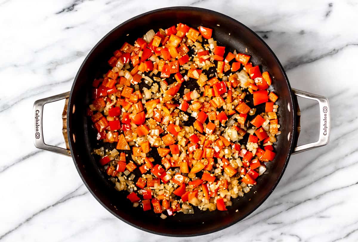 Peppers and onions cooking in a black skillet.