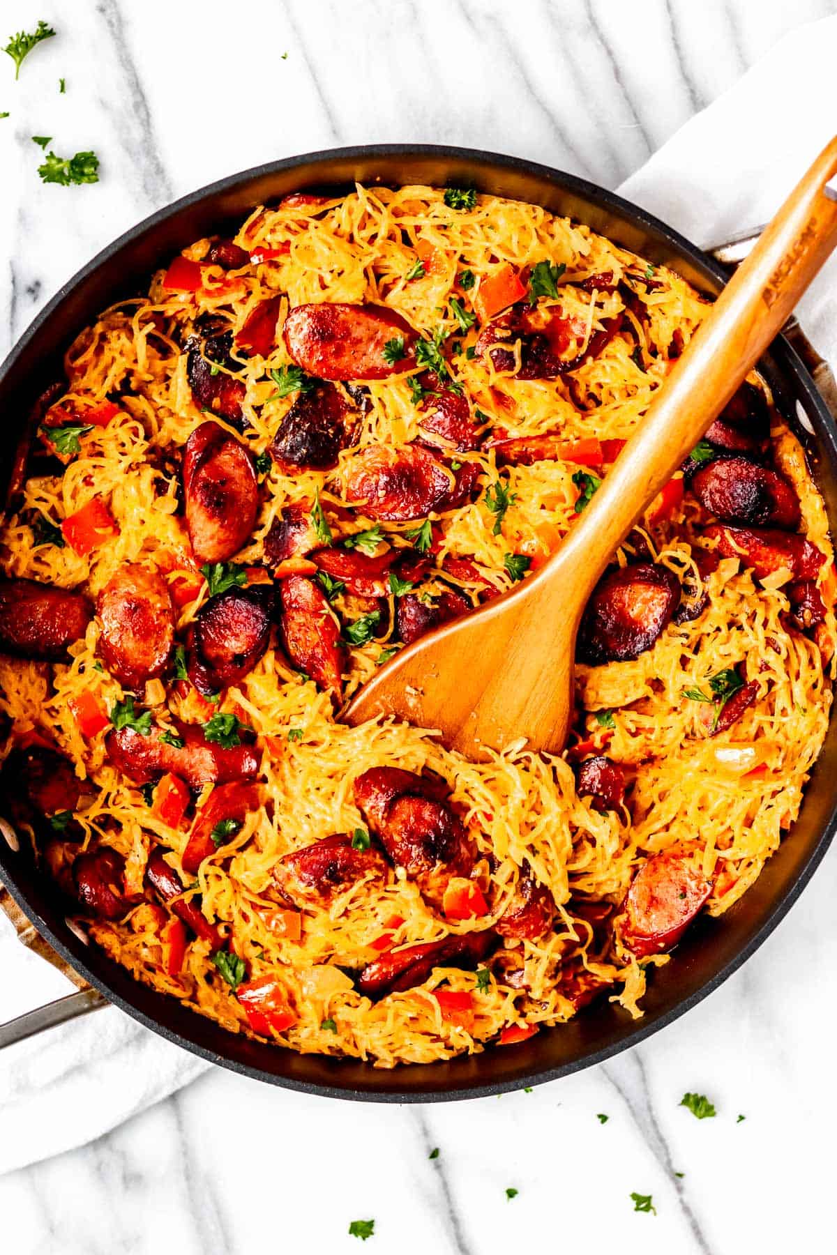 Italian Sausage Spaghetti Squash Skillet with a wood server in it over a white towel and background.