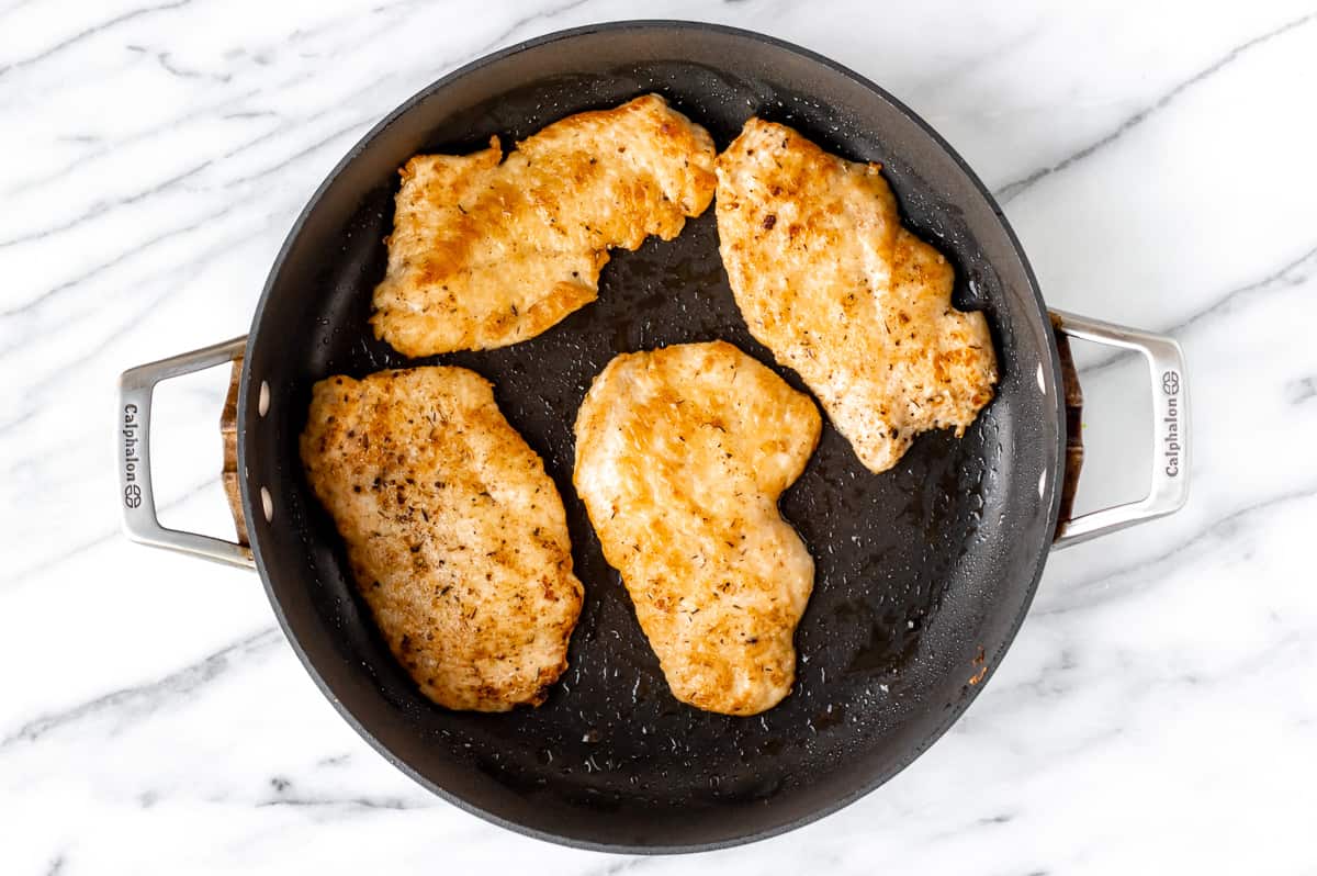 Four chicken breasts cooked in a black skillet.