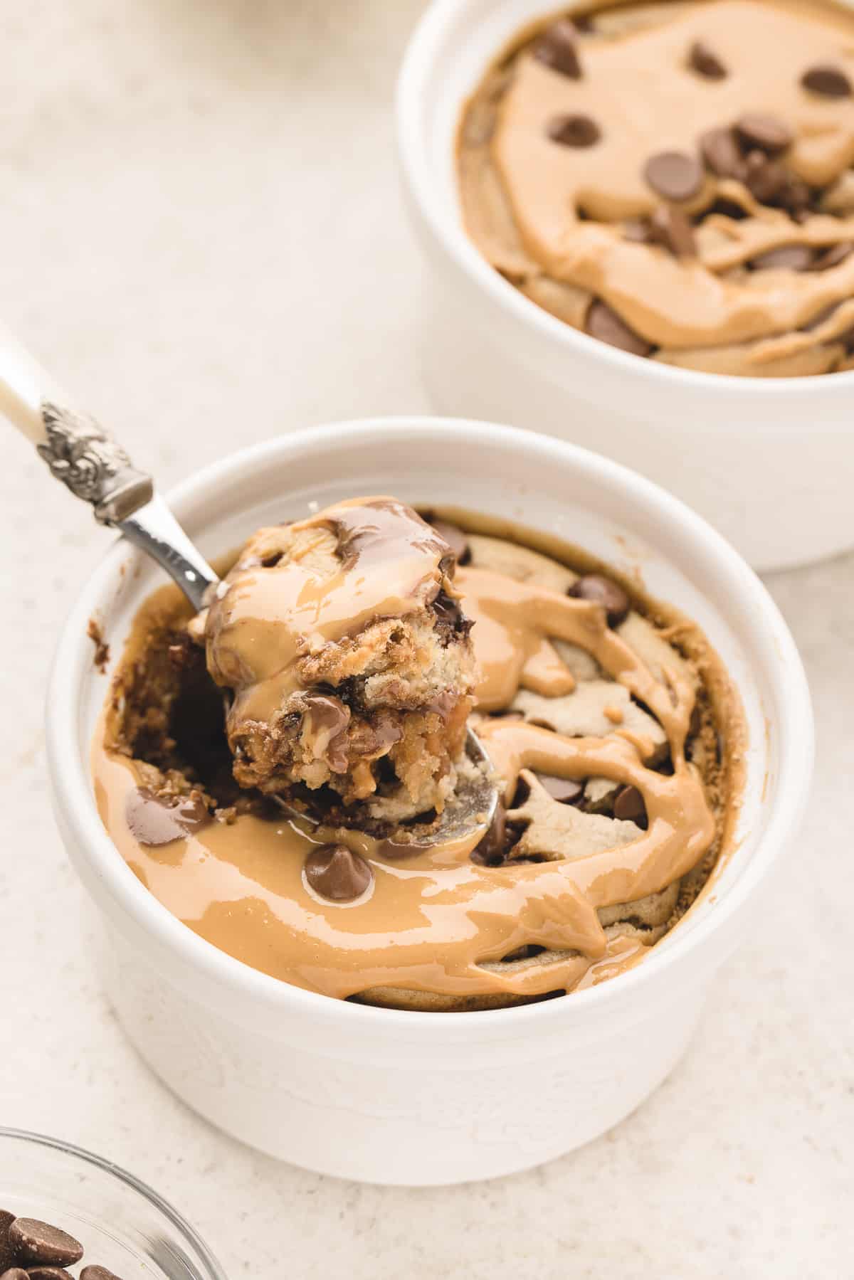 A spoonful of peanut butter chocolate blended baked oats being lifted up from a ramekin with a second ramekin in the background.