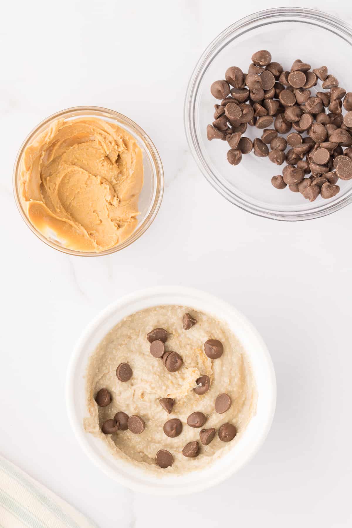 Blended oatmeal topped with chocolate chips in a ramekin with small bowls of peanut butter and chocolate chips around it.