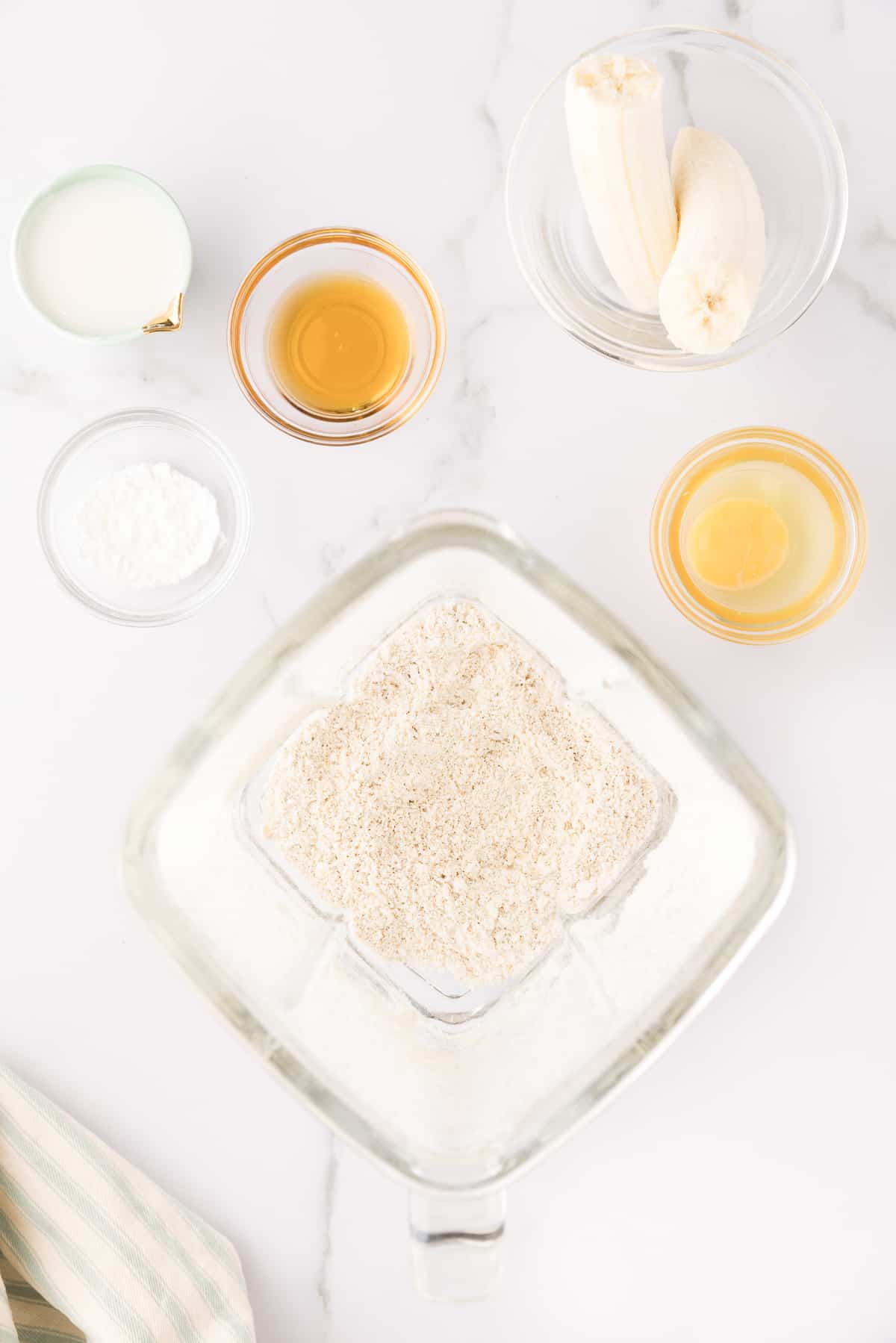 Overhead of blended oats in a blender with other ingredients in bowls around it.