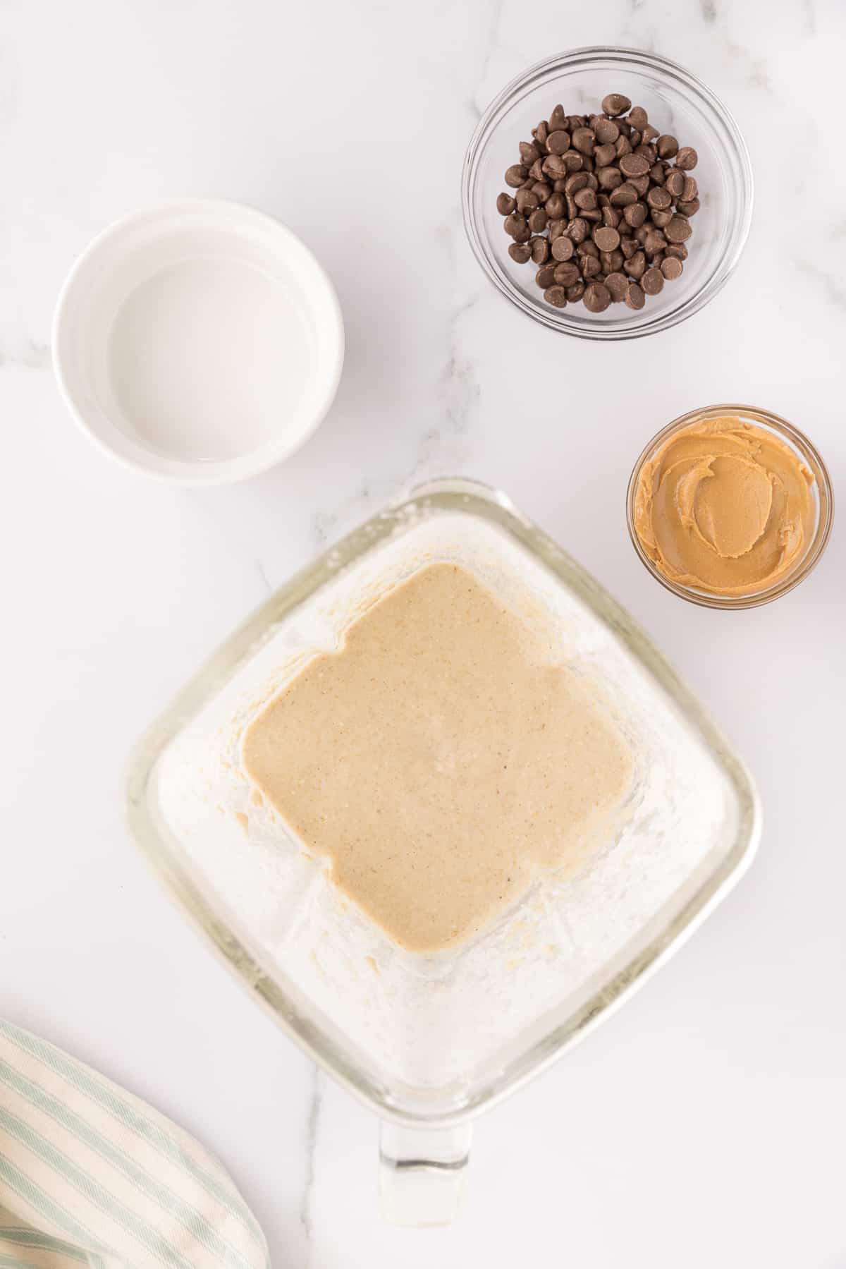 Blended oatmeal in a blender with other ingredients in bowls around it.