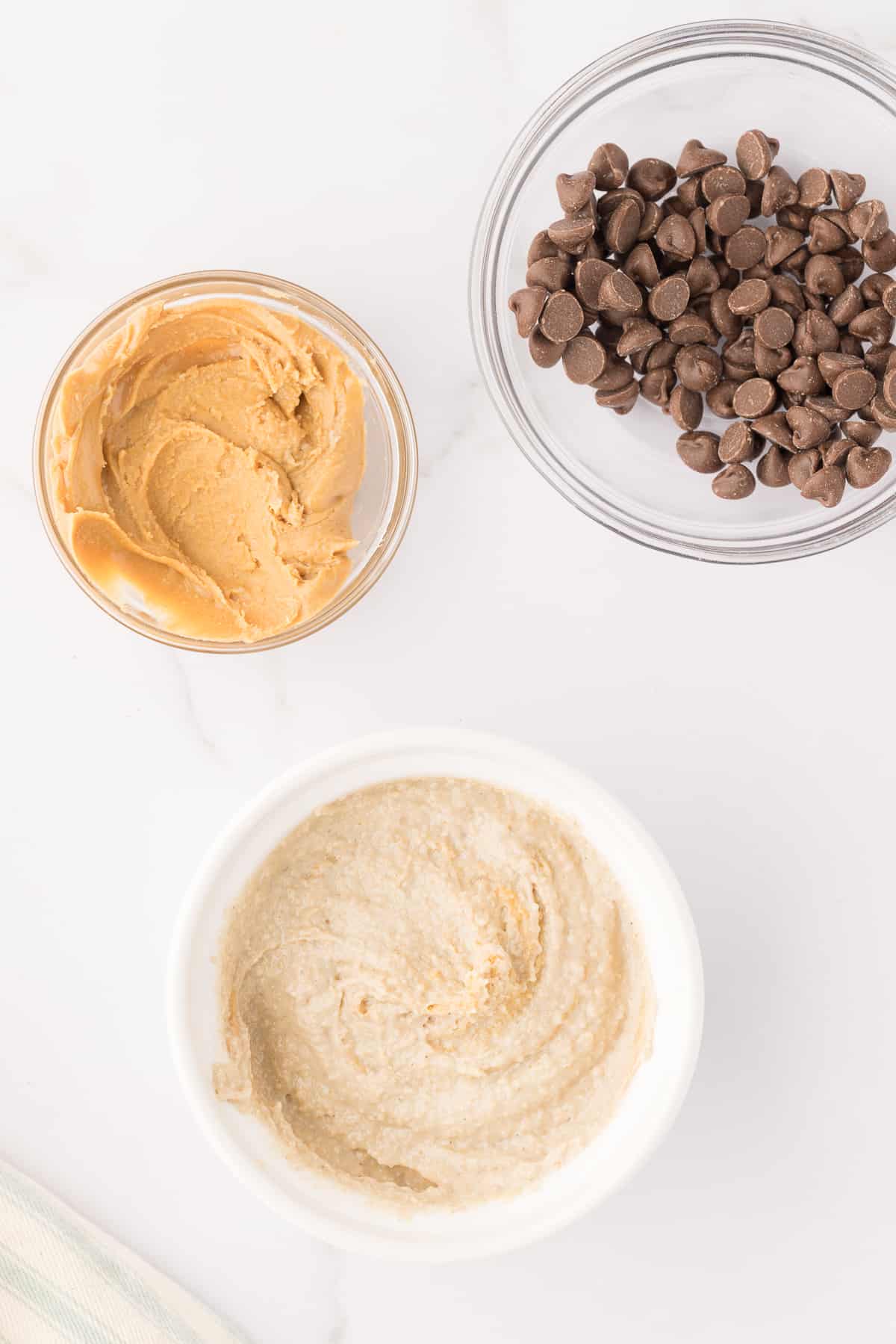 Peanut butter blended oatmeal in a ramekin with small bowls of peanut butter and chocolate chips around it.