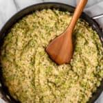 A wood turner in a skillet of cheesy broccoli cauliflower rice with text overlay that says cheesy broccoli cauliflower rice.