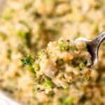A forkful of cheesy broccoli cauliflower rice being held up over a bowl full of more of the same with text overlay that says cheesy broccoli cauliflower rice.