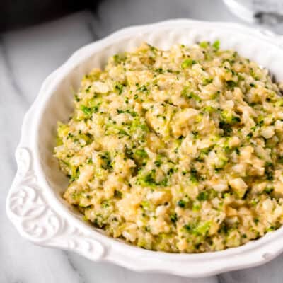 Close up of cheesy broccoli cauliflower rice in a white bowl.