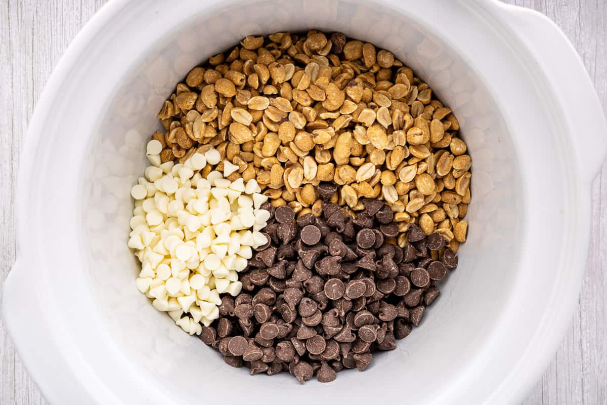 Peanuts, white chocolate chips and milk chocolate chips in a crock pot.