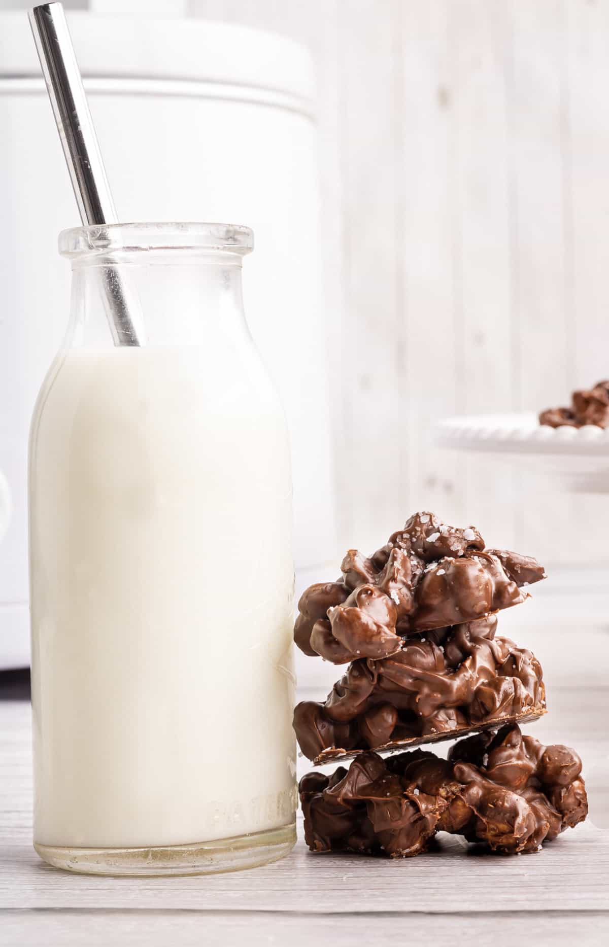A stack of chocolate peanut clusters next to a glass of milk with a straw in it.