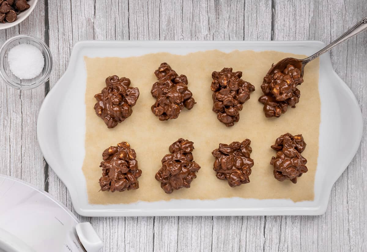Peanut clusters being spooned onto a parchment lined tray.