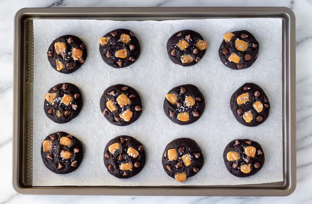 Baked dark chocolate salted caramel cookies on a parchment paper lined baking sheet.