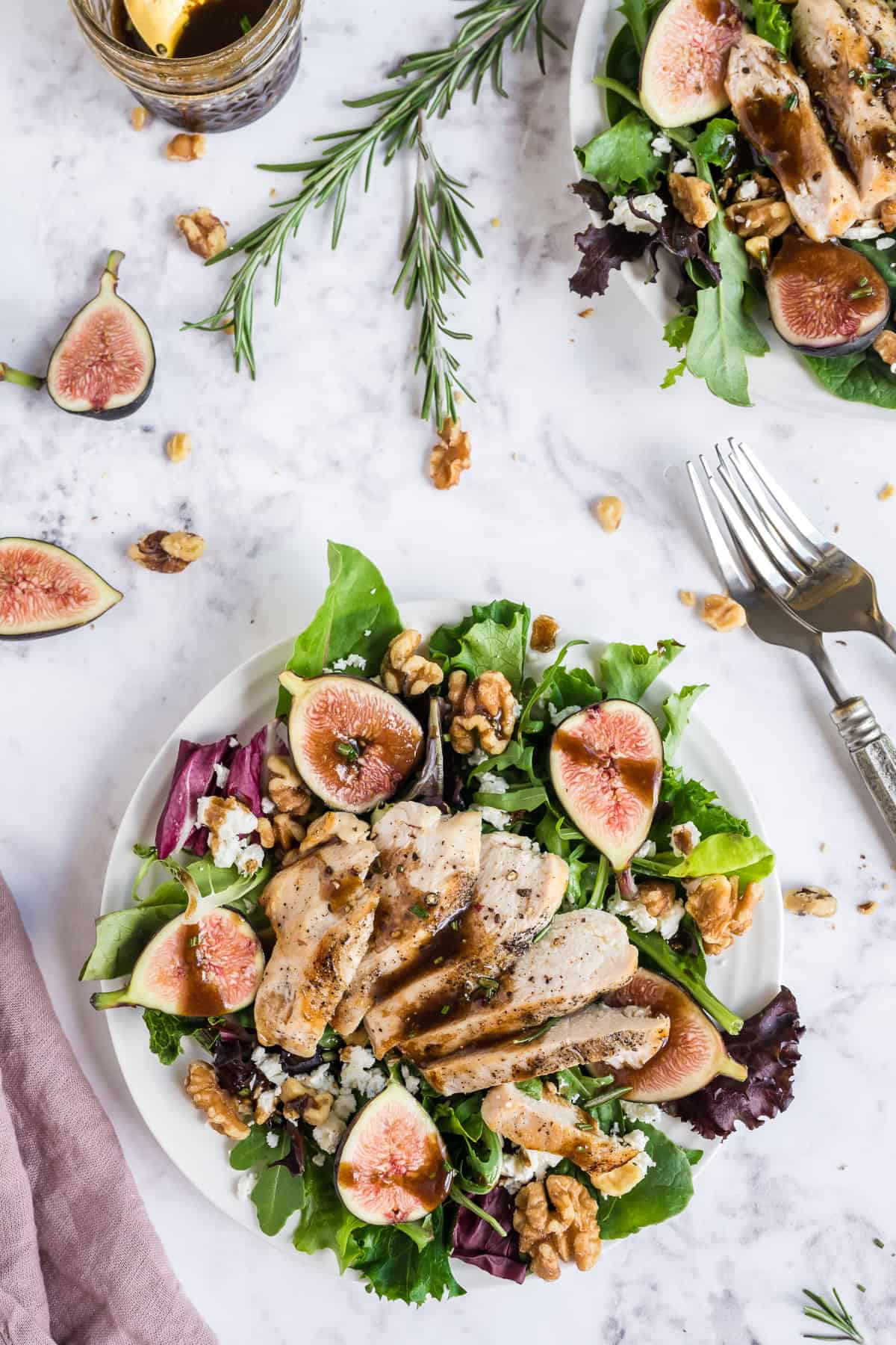 Overhead of a salad with figs and chicken with extra figs, chicken, walnuts and rosemary around it.
