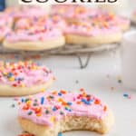 A sugar cookie with pink frosting and rainbow sprinkles with a bite taken out of it and more cookies in the background. Text overlay reads Lofthouse Cookies.