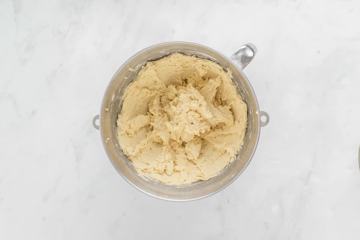 Sugar cookie dough in a silver mixing bowl on a white background.