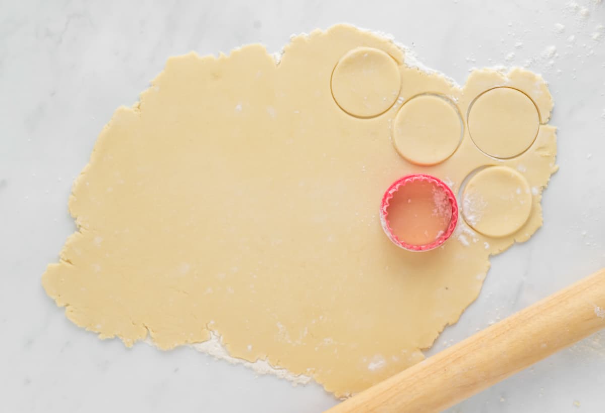 Circular cookies being cut out of rolled dough with a cookie cutter.