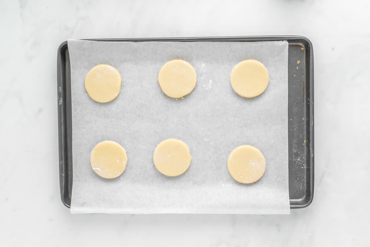 Six cookie dough cut outs on a parchment paper lined baking sheet.
