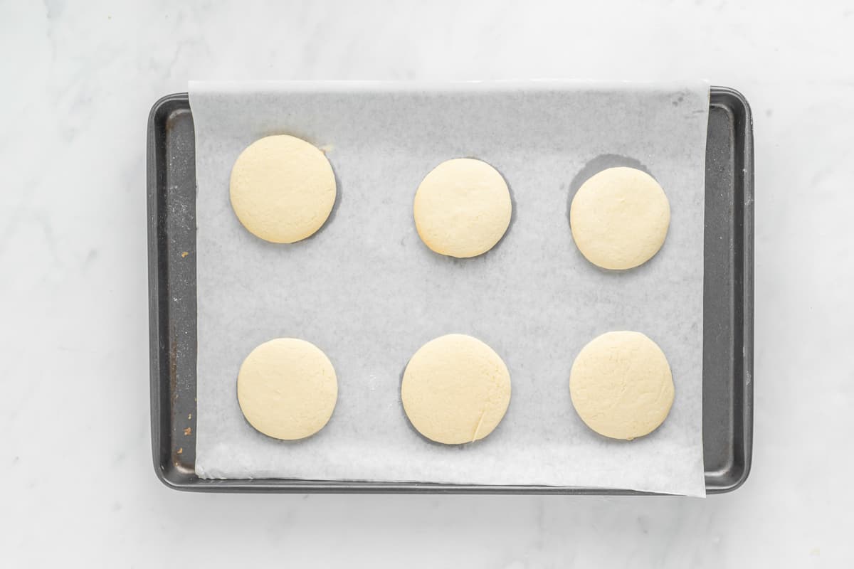 Six baked sugar cookies on a parchment paper lined baking sheet.