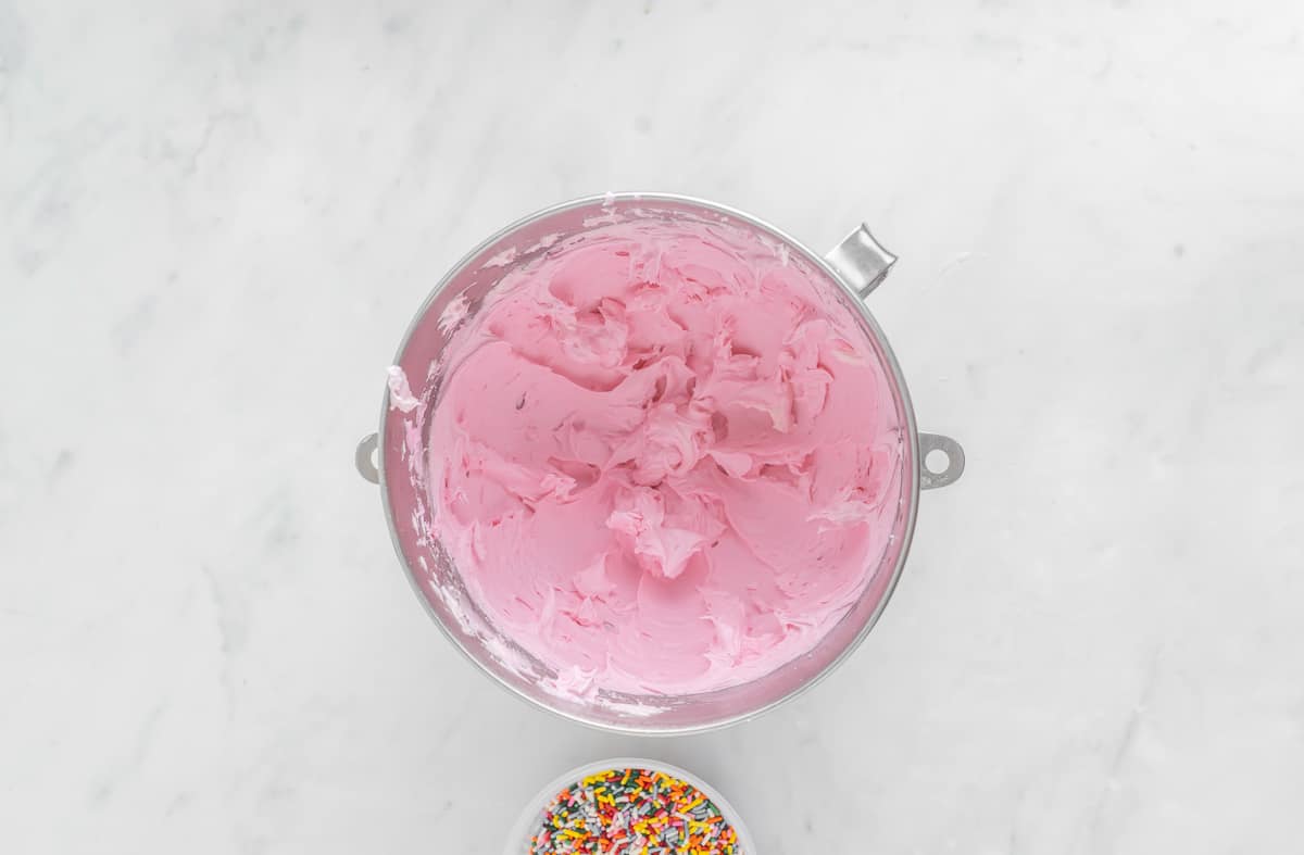 Pink buttercream frosting in a silver mixing bowl over a white background.