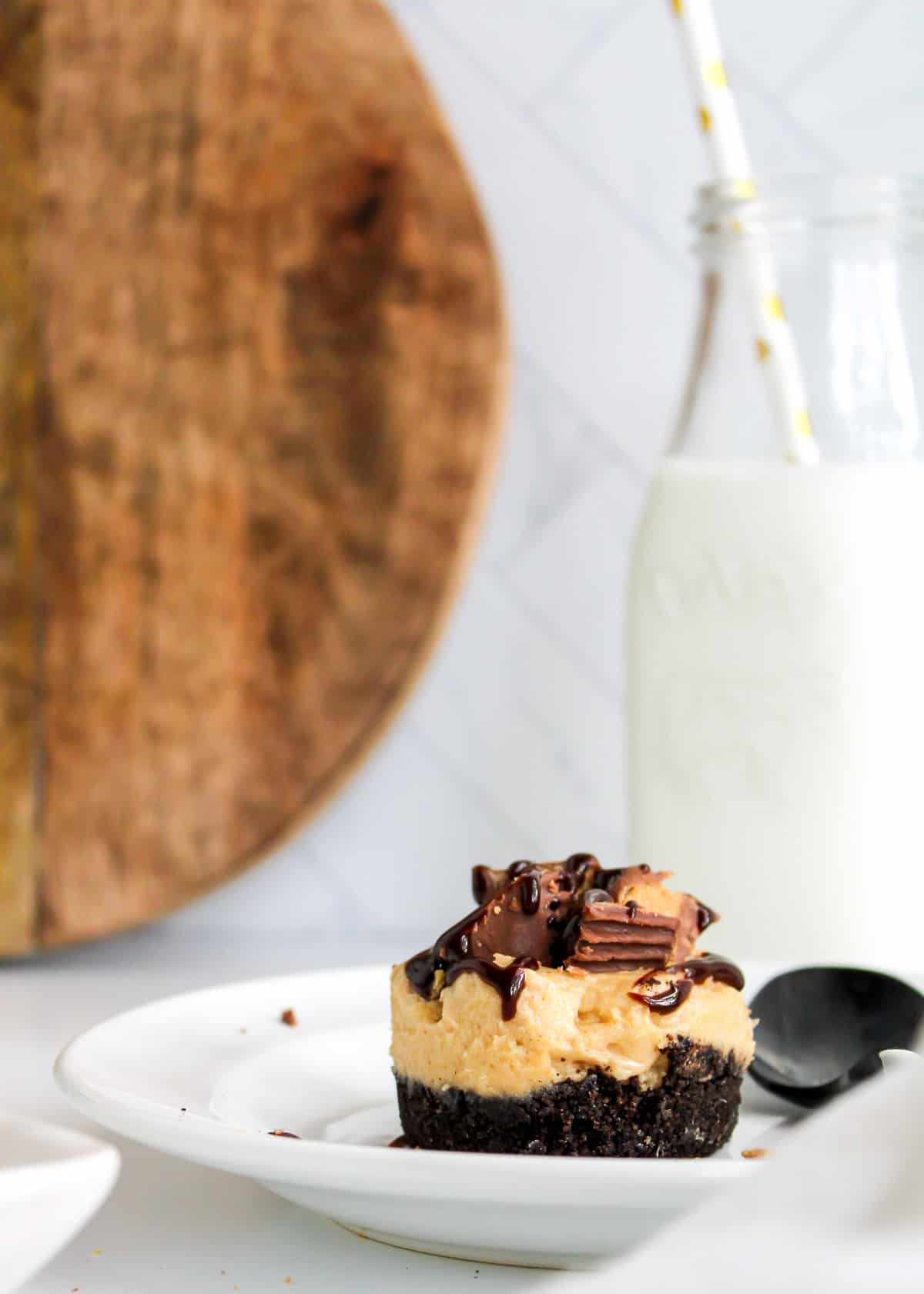 A mini peanut butter pie on a white plate with a bottle of milk and wood cutting board in the background.