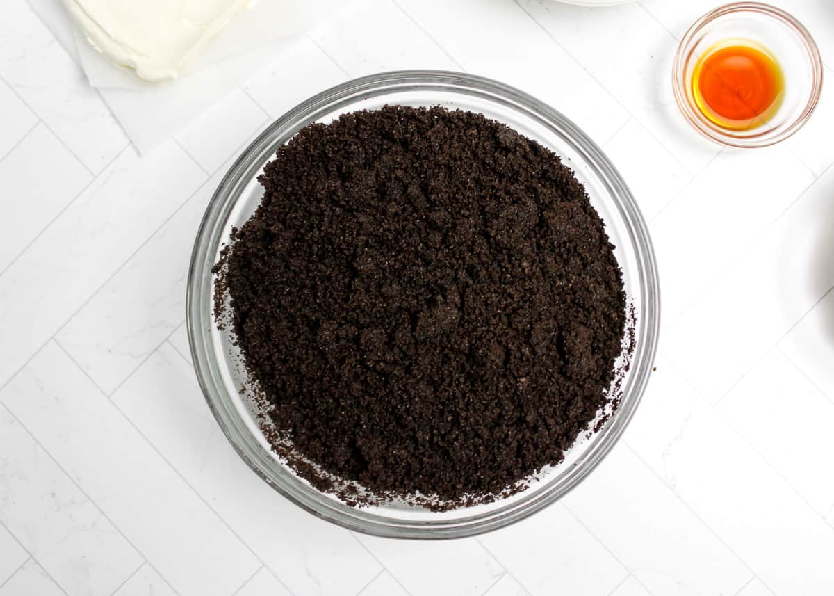 Oreo crumbs in a glass bowl over a white background.