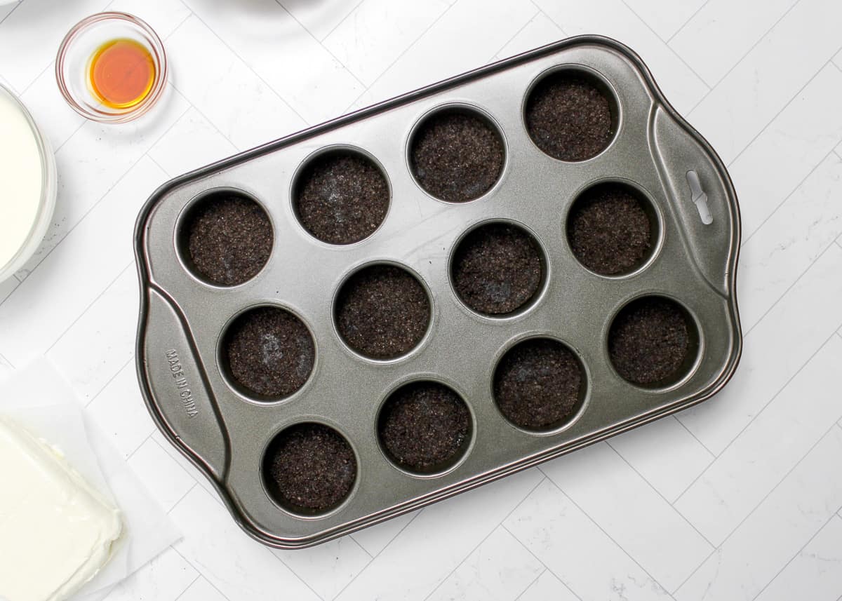 Oreo crumbs pressed into a muffin tin.