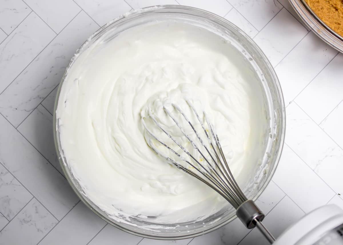 Whipped cream in a glass bowl with a whisk in it.