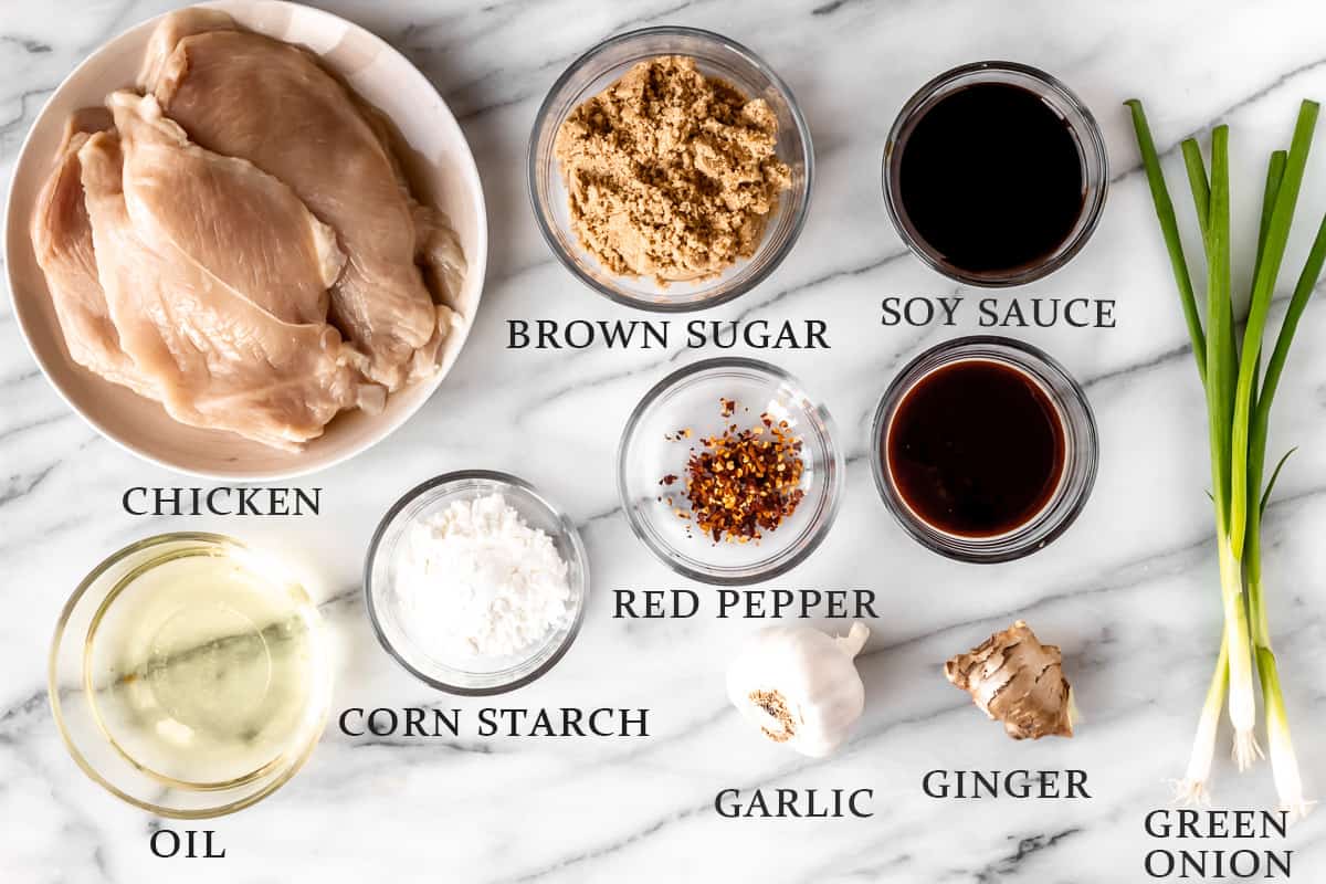 Ingredients needed to make Mongolian chicken in bowls on a marble backdrop with text overlay stating all of the individual ingredients.