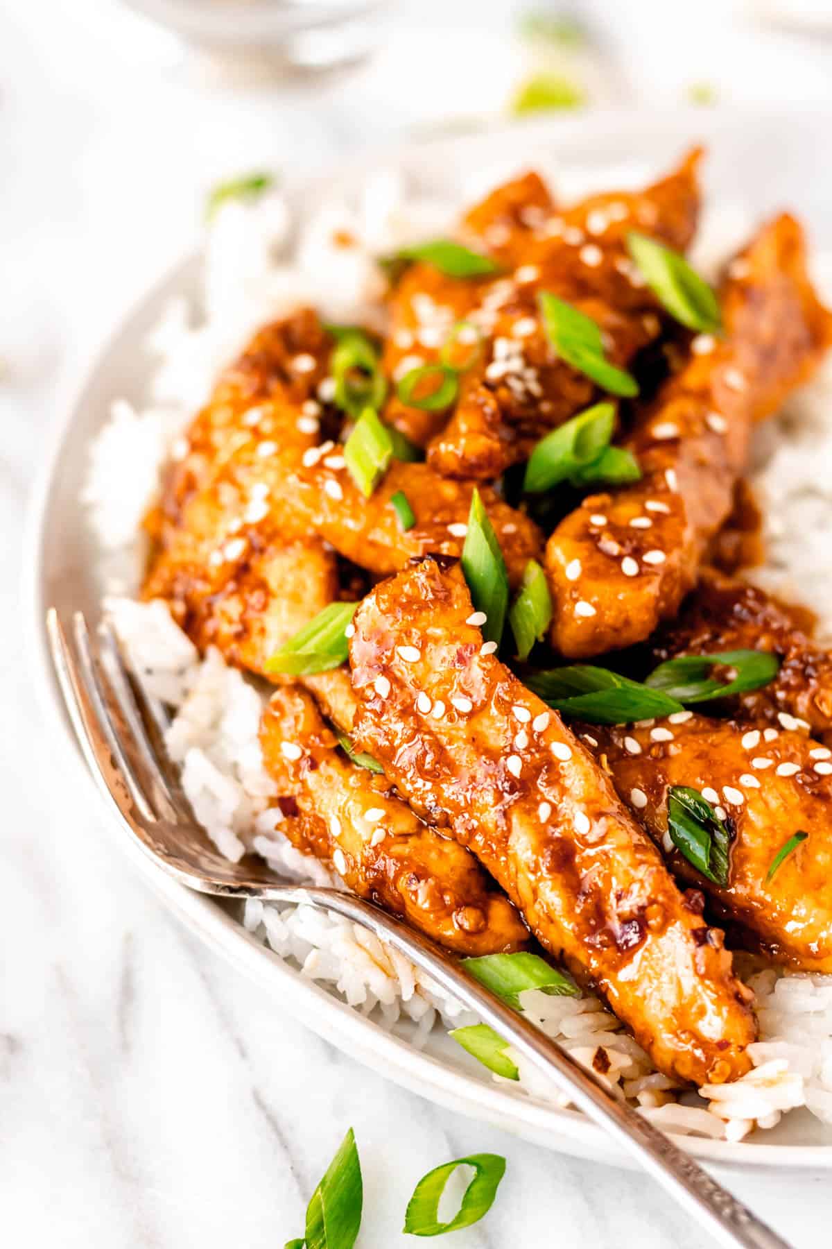 Close up of Mongolian chicken strips with green onions and sesame seeds as garnish over white rice.