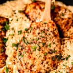 Close up of Parmesan Chicken Orzo in a skillet with a wood spoon lifting up a piece of chicken with text overlay.