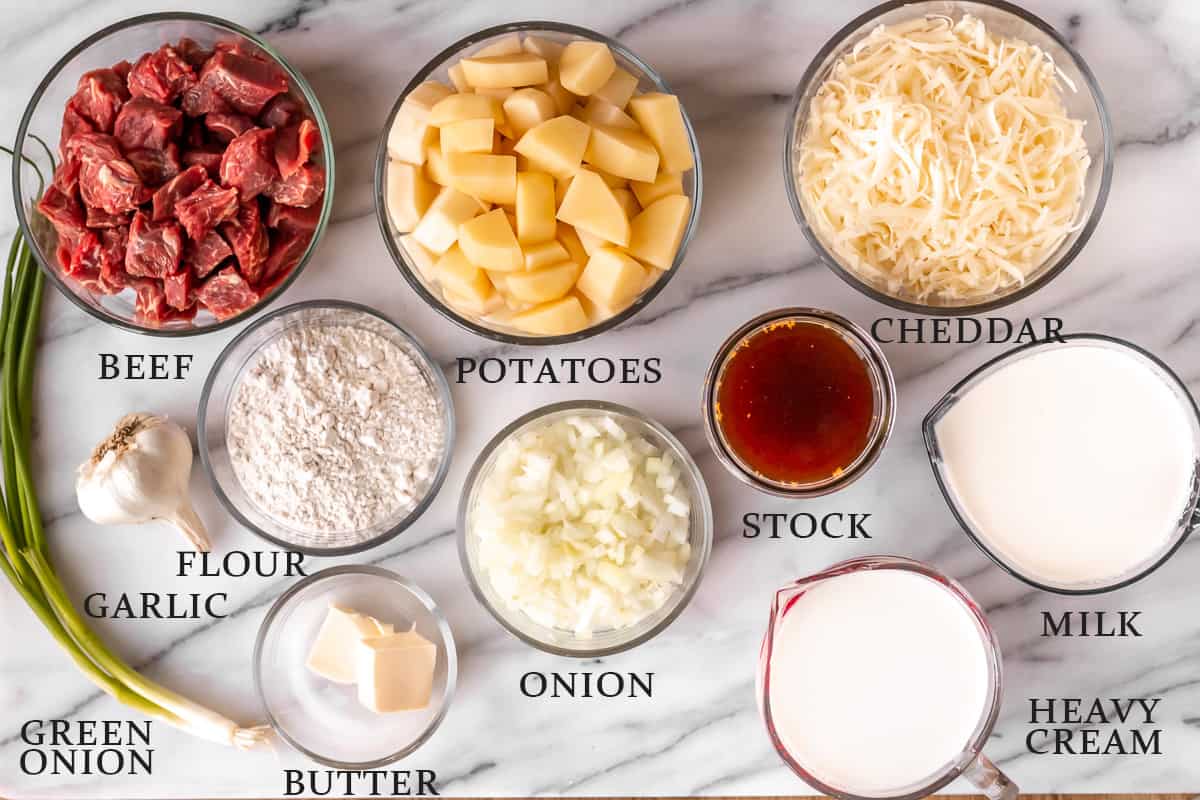 Ingredients needed to make steak and potato soup on a marble background with text overlay.