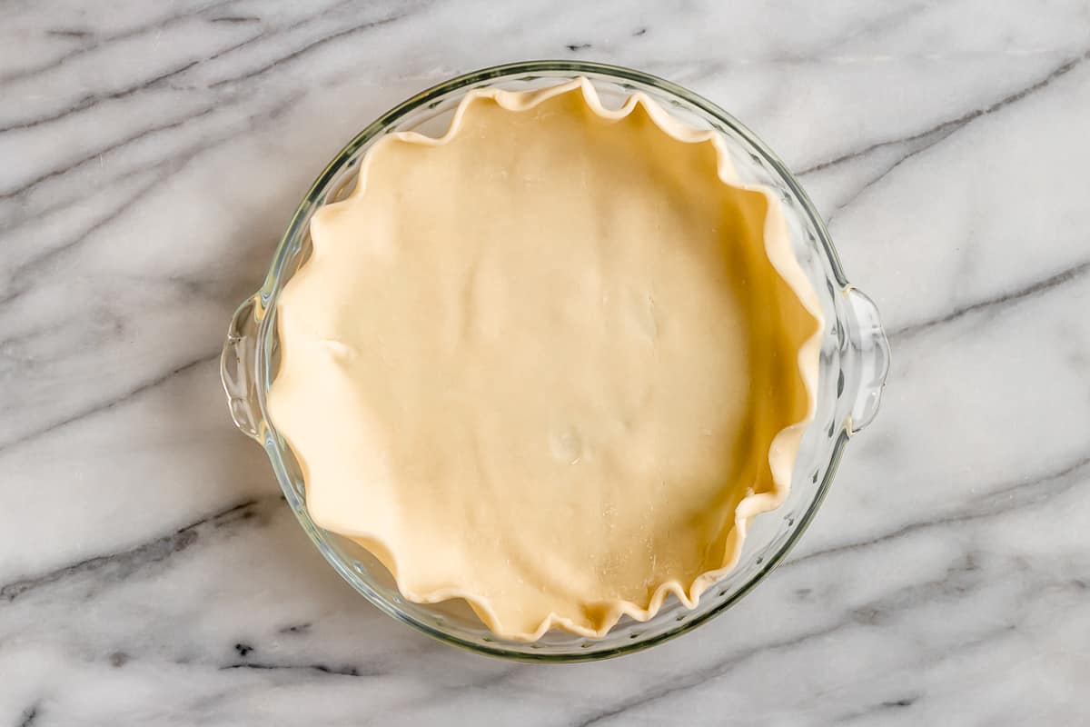 A pie crust in a pie pan on a marble background.