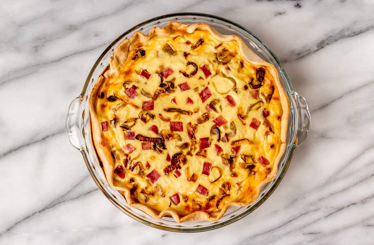 Baked ham and cheese quiche on a marble background.