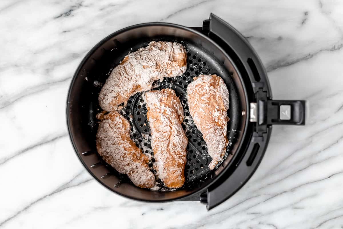 Four floured chicken tenders in the bottom of an air fryer basket.