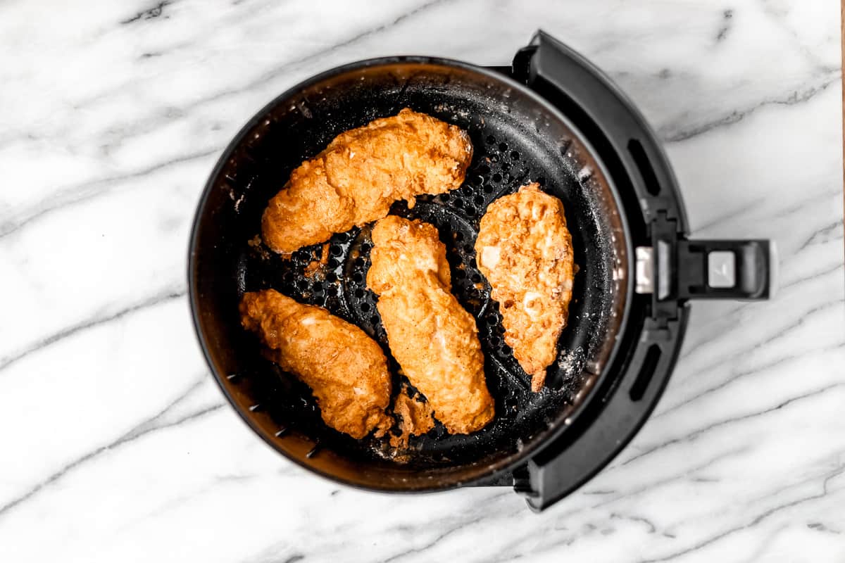 Four air fried chicken tenders in the bottom of an air fryer basket.
