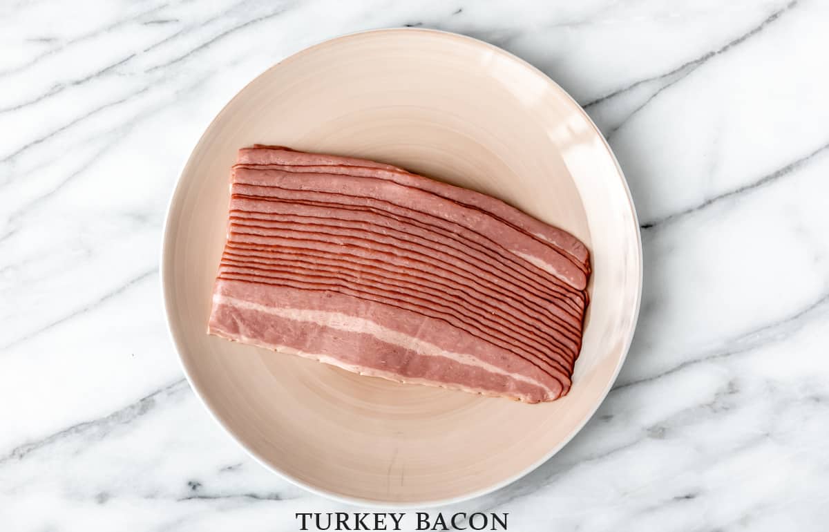 Uncooked turkey bacon on a tan plate.